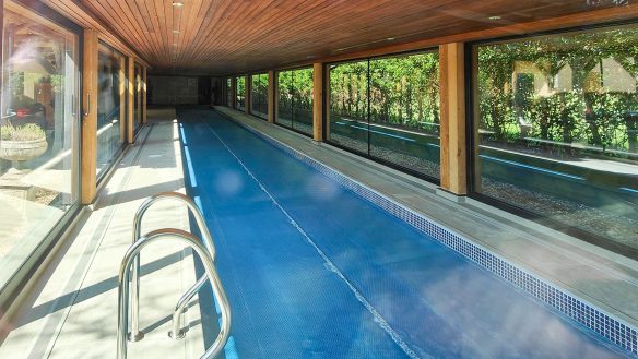 indoor long swimming pool with large windows looking out to gardens