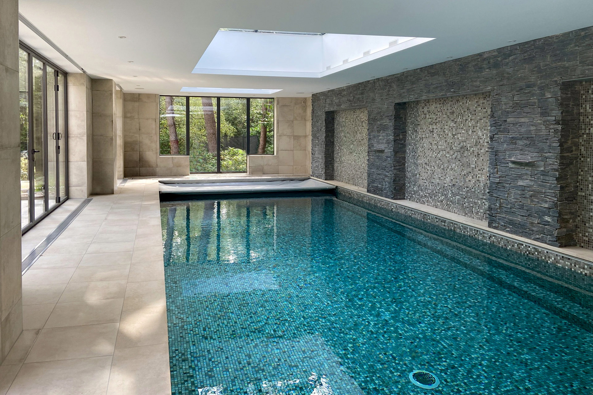 indoor swimming pool with stone wall and roof light above pool