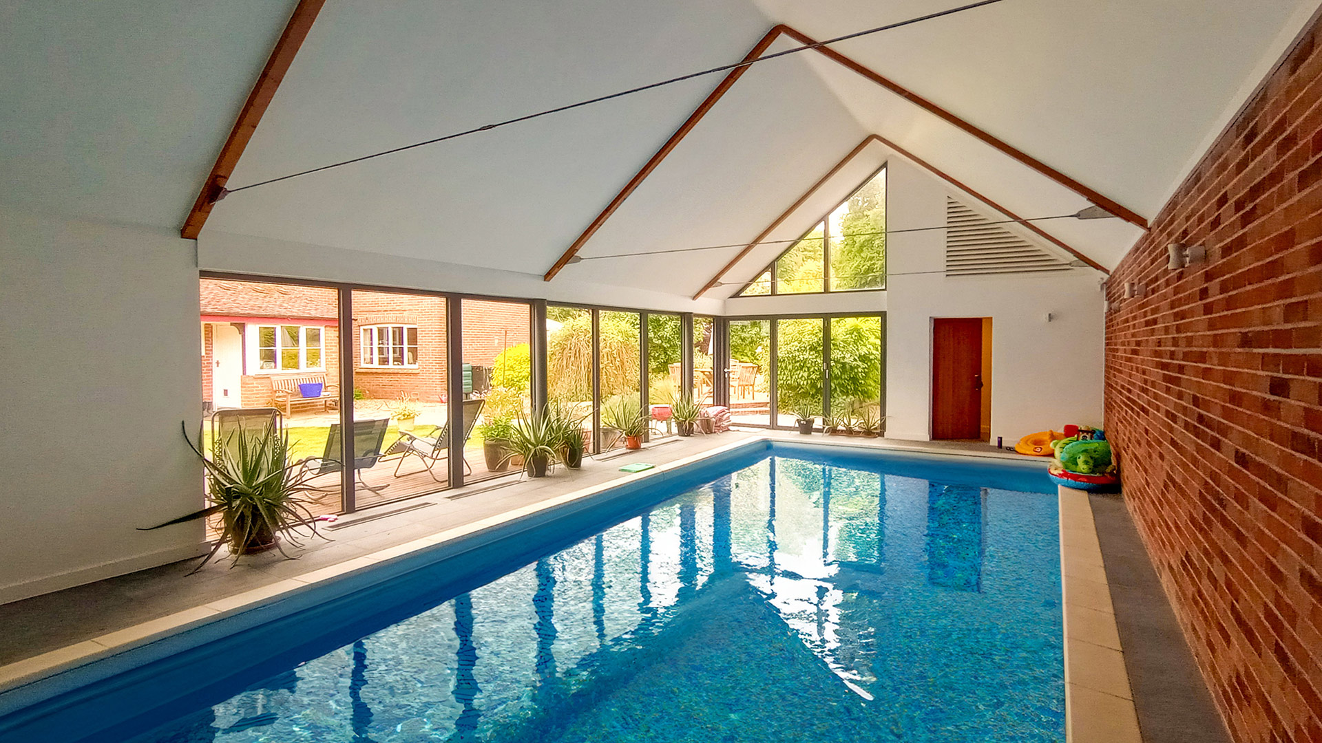 indoor swimming pool with vaulted ceiling and windows overlooking garden