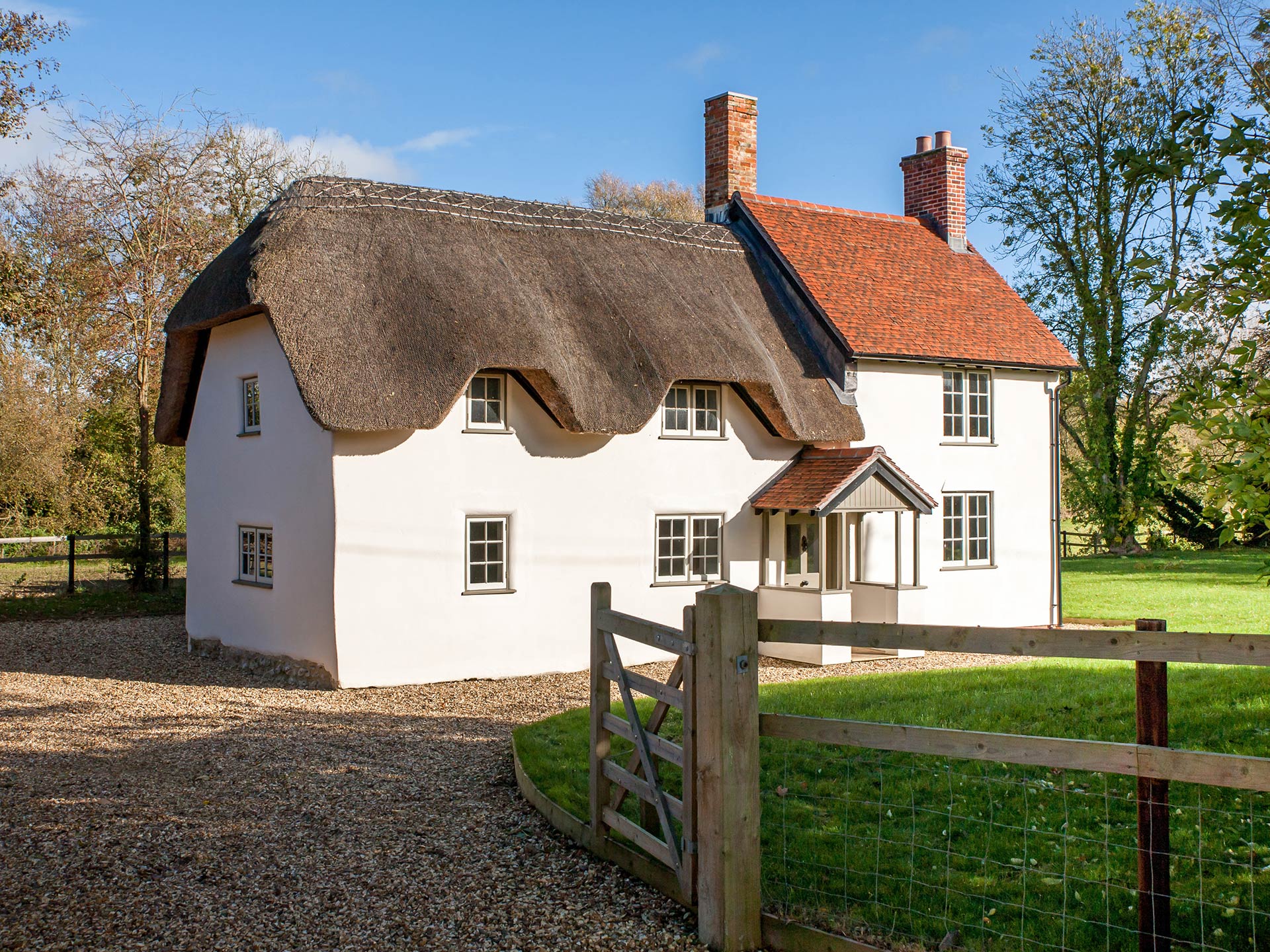 approach view of detached thatched house with shingle driveway