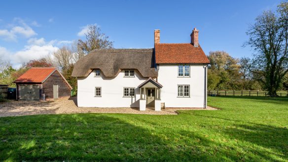 front elevation of detached house with thatched roof and detached garage