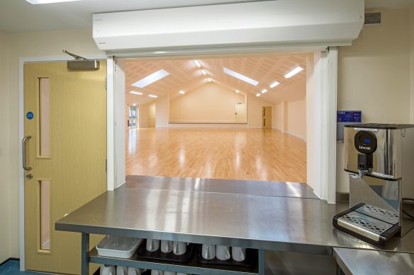 village hall kitchen with hatch looking out to large hall area with vaulted ceiling