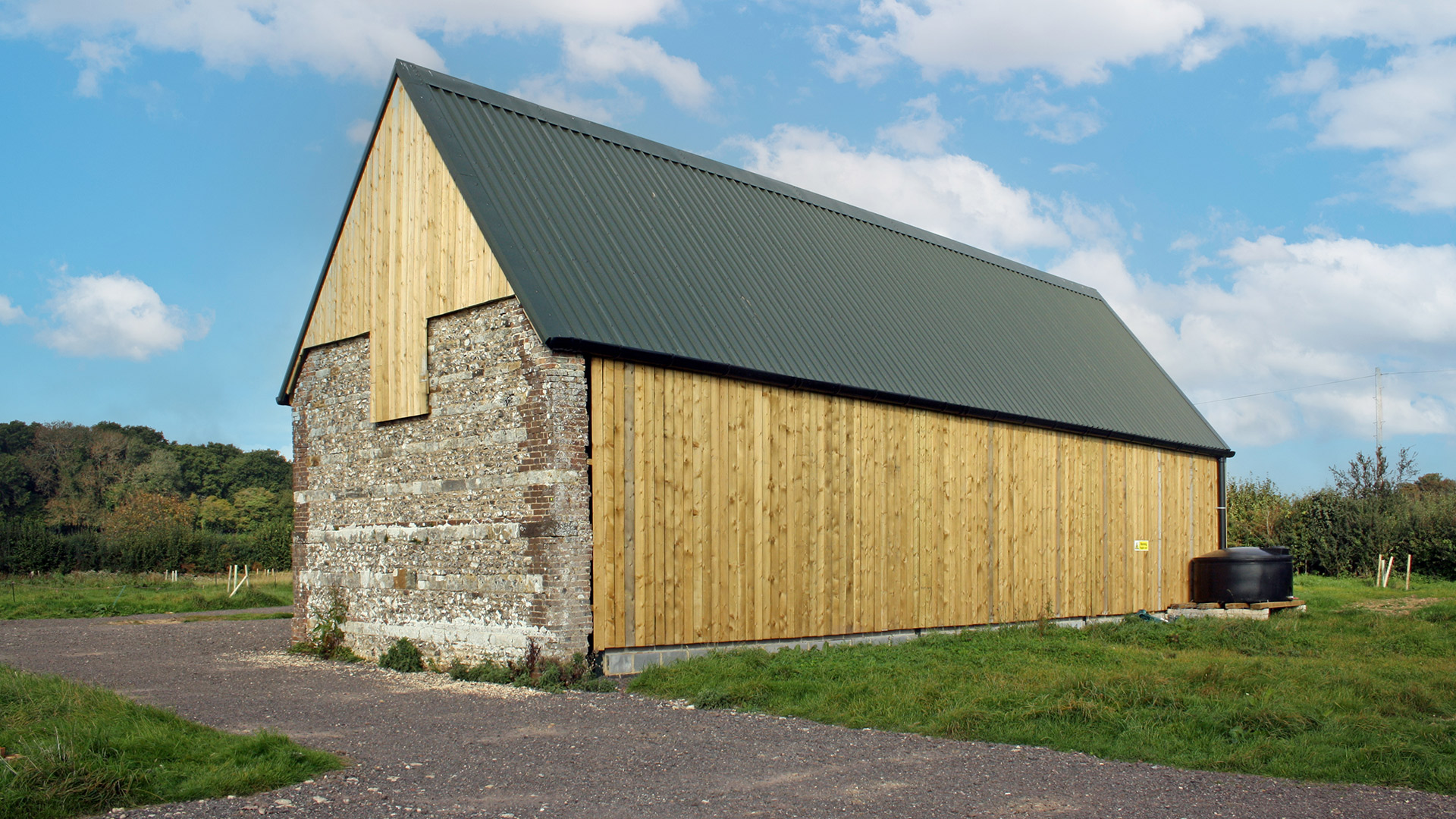 rear view of agricultural steal framed barn with timber cladding and stone wall